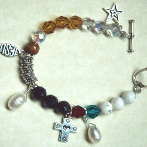 May include: A silver charm bracelet with a variety of charms, including a cross, a fish, a star, and hearts. The bracelet is made with brown, black, white, and clear beads.
