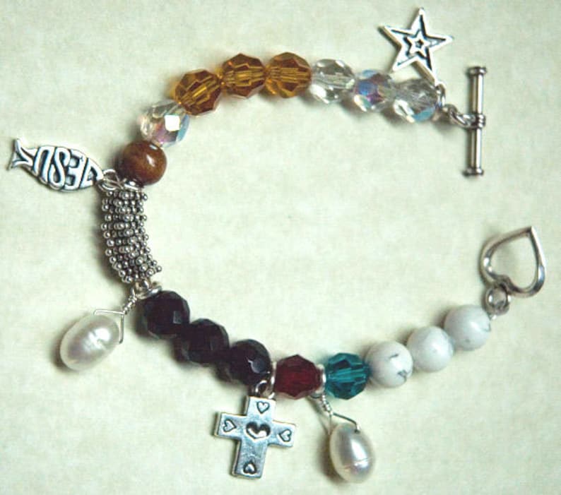 May include: A silver charm bracelet with a variety of charms, including a cross, a fish, a star, and hearts. The bracelet is made with brown, black, white, and clear beads.