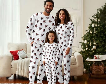 May include: Matching family pajamas in white with a repeating pattern of black and red Mickey Mouse heads. The pajamas include long-sleeved tops and pants. A Christmas tree is in the background.
