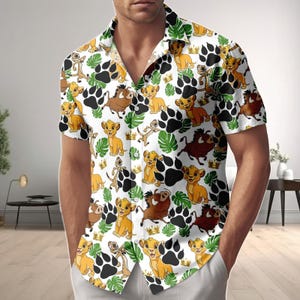 May include: White button-down shirt with a repeating pattern of cartoon lion cubs, crowns, paw prints, and tropical leaves. The short-sleeved shirt features a classic collar and a relaxed fit, perfect for casual wear.