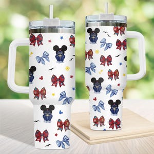 Puede incluir: Dos vasos térmicos blancos con asas, tapas y pajitas. Los vasos presentan un estampado de lazos rojos y azules, barcos de crucero con forma de Mickey Mouse, estrellas y elementos náuticos.