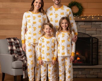 May include: Matching family pajama sets in white with a yellow animal and moon pattern. The long-sleeved tops and pants have yellow cuffs and trim. A family of four is wearing the pajamas in front of a fireplace.
