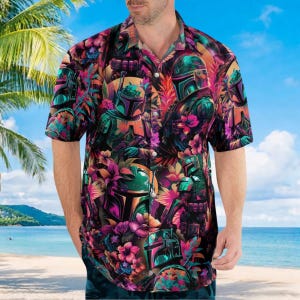 Op de afbeelding: Korte mouwen button-down shirt met een levendig tropisch bloemen- en karakterontwerp. Het shirt heeft een kleurrijk patroon van bloemen en een karakter in tinten groen, paars en oranje. Het shirt wordt door een persoon op een strand gedragen.