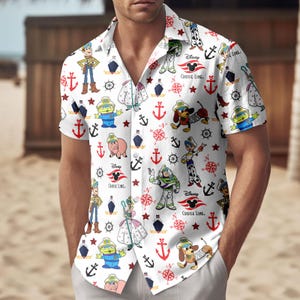 Könnte beinhalten: Weißes kurzärmeliges Hemd mit einem sich wiederholenden Muster von Disney's Toy Story-Charakteren, Ankern, Sternen und Kompassen. Das Hemd hat eine Knopfleiste und einen Kragen. Das Disney Cruise Line-Logo ist ebenfalls sichtbar.