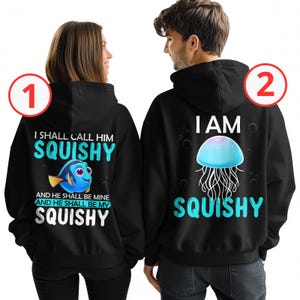 May include: A matching pair of black hoodies with a blue and turquoise graphic print. One hoodie features a cartoon Dory fish with the text "I shall call him squishy and he shall be mine and he shall be my squishy". The other hoodie features a blue jellyfish with the text "I am squishy".