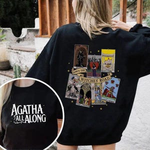 May include: Black sweatshirt with a graphic print of tarot cards. The text "Witches Road" is printed in gold lettering. The text "Agatha All Along" is printed on the front of the shirt in white lettering.