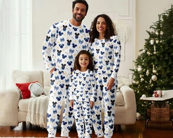 May include: Matching family pajama sets in white with a pattern of blue Mickey Mouse heads and bows. The long-sleeved tops and pants are worn by a family of three in a cozy living room setting, with a Christmas tree in the background.