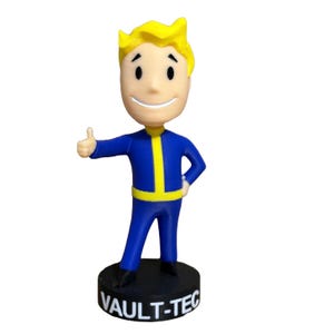 May include: A blue and yellow Vault-Tec bobblehead figurine of a smiling person with blonde hair giving a thumbs up.