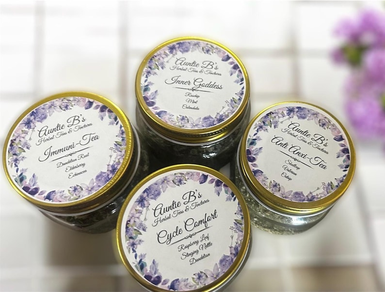 Puede incluir: Cuatro frascos de vidrio de t&eacute; de hierbas con tapas doradas. Cada frasco tiene una etiqueta con el texto "Auntie B's Herbal Teas & Tinctures" y un nombre de t&eacute; diferente. Las etiquetas tienen un dise&ntilde;o floral.