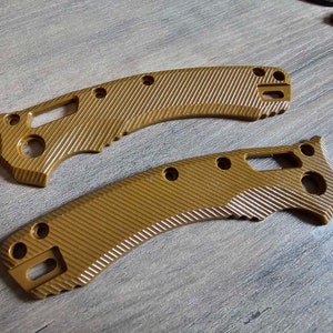 Puede incluir: Dos cachas de cuchillo de color marrón claro con un patrón de rayas diagonales texturizadas. Cada cacha tiene múltiples agujeros y un recorte para tornillos y otros herrajes. Las cachas están diseñadas para un cuchillo plegable.