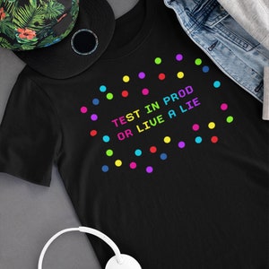 Peut inclure: T-shirt noir avec le texte "TEST IN PROD OR LIVE A LIE" en couleurs arc-en-ciel. Le t-shirt est décoré de points colorés.