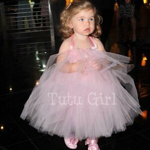 Pu&ograve; includere: Una bambina che indossa un abito tutu di tulle rosa con un nastro di raso e un fiocco di fiori. L'abito ha una gonna ampia ed &egrave; perfetto per un'occasione speciale. Il testo "Tutu Girl" &egrave; stampato sulla gonna.
