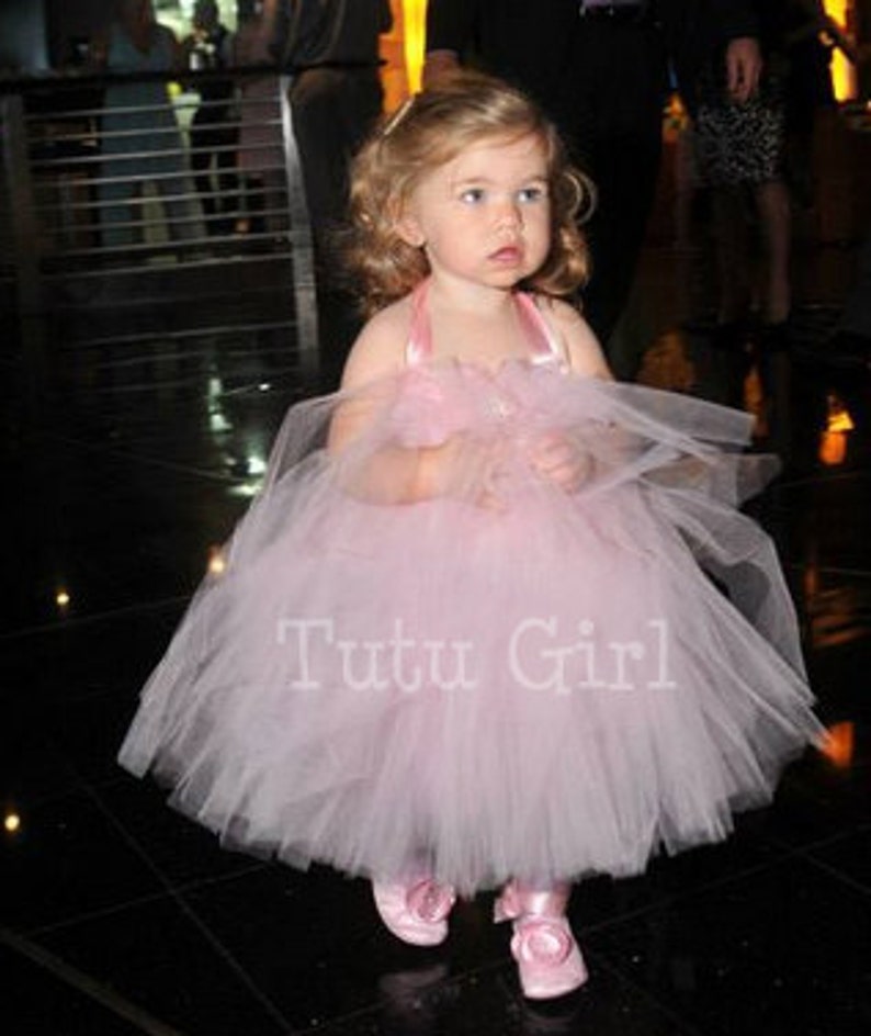 Pu&ograve; includere: Una bambina che indossa un abito tutu di tulle rosa con un nastro di raso e un fiocco di fiori. L'abito ha una gonna ampia ed &egrave; perfetto per un'occasione speciale. Il testo "Tutu Girl" &egrave; stampato sulla gonna.