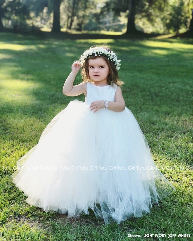 Peut inclure: Une jeune fille portant une robe en tulle blanche et une couronne de fleurs. La robe a une jupe ample et est parfaite pour une occasion sp&eacute;ciale.