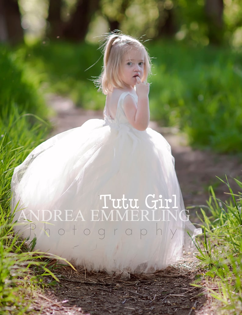 Peut inclure: Une jeune fille portant une robe en tulle blanche et un bandeau blanc, debout sur un chemin dans une zone herbeuse. Le texte "Tutu Girl Andrea Emmerling Photography" est visible sur la robe.