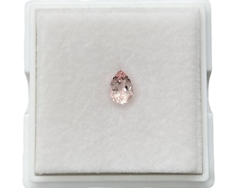 Puede incluir: Una piedra preciosa rosa en forma de pera en una caja forrada de terciopelo blanco.