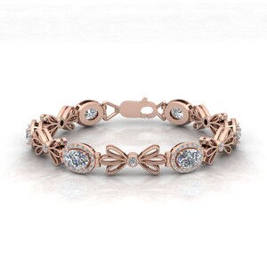 May include: A rose gold bracelet with oval-shaped diamonds set in a halo setting. The bracelet features a delicate bow design with smaller diamonds.