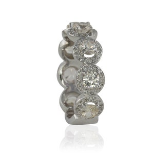 Puede incluir: Un anillo plateado con m&uacute;ltiples piedras preciosas redondas y transparentes. Cada gema est&aacute; rodeada de piedras m&aacute;s peque&ntilde;as y transparentes, creando un efecto de halo. El anillo se encuentra sobre un fondo blanco, con un ligero reflejo.