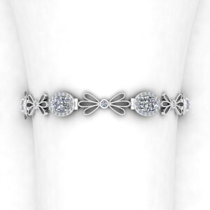 May include: A silver bracelet with a delicate bow design and oval-shaped gemstones. The bracelet is adorned with smaller gemstones around the larger stones.