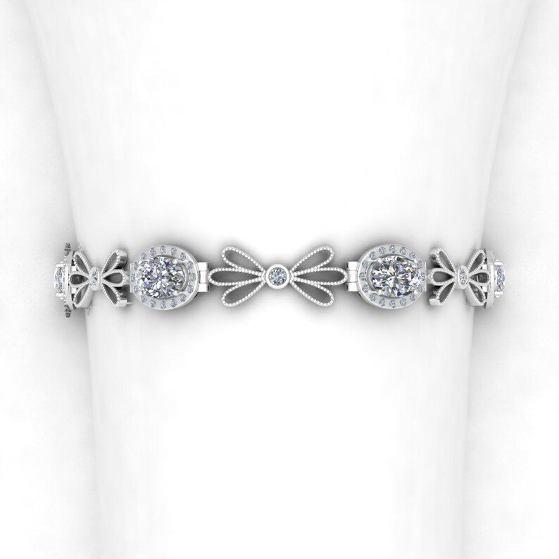 May include: A silver bracelet with a delicate bow design and oval-shaped gemstones. The bracelet is adorned with smaller gemstones around the larger stones.