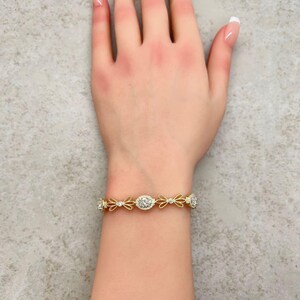 May include: A gold bracelet with a delicate design featuring small, clear stones and bow-shaped accents.