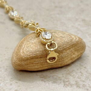 May include: A gold bracelet with a delicate floral design and clear cubic zirconia stones. The bracelet has a lobster claw clasp.