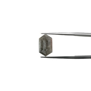 Può includere: Un diamante grigio a forma di ottagono tenuto da una pinzetta su uno sfondo bianco.