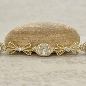 May include: A gold bracelet with a central oval-shaped diamond surrounded by smaller diamonds. The bracelet is decorated with bow-shaped accents on either side of the diamond.