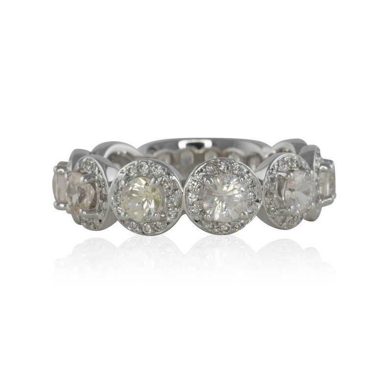 Puede incluir: Un anillo de plata con una serie de piedras preciosas redondas y transparentes, cada una rodeada de piedras m&aacute;s peque&ntilde;as y brillantes. El dise&ntilde;o del anillo es sim&eacute;trico, con las piedras espaciadas uniformemente. Fondo blanco.