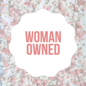 May include: A white cloud-shaped sign with the text "WOMAN OWNED" in pink letters against a background of white and pink flowers.