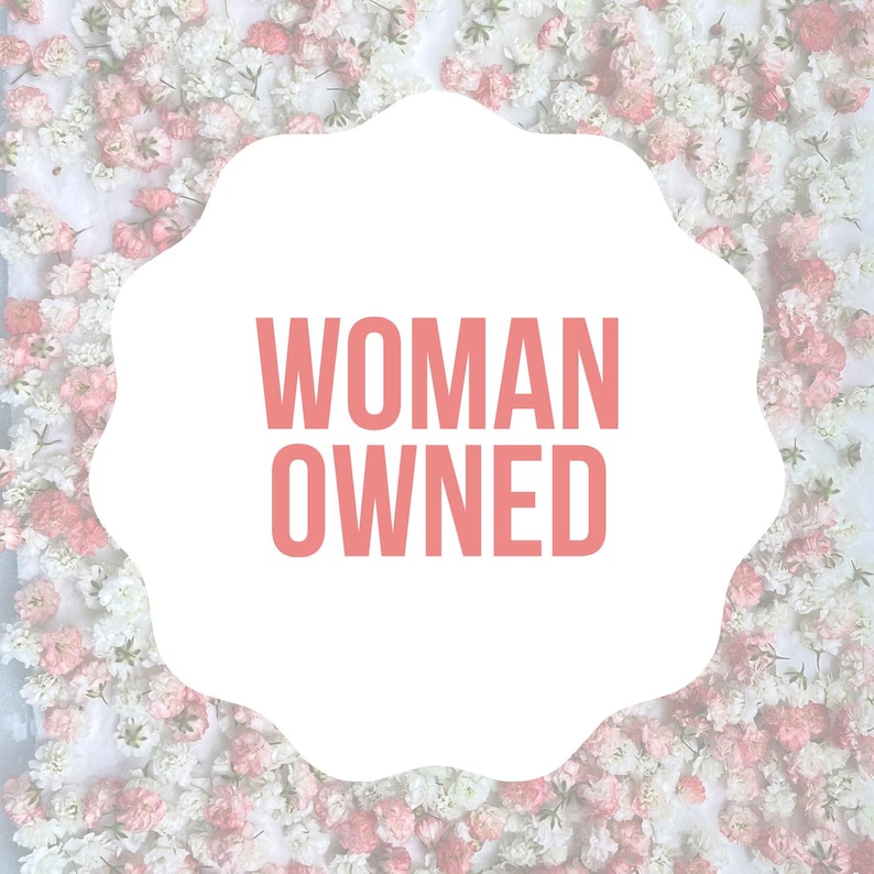 May include: A white cloud-shaped sign with the text "WOMAN OWNED" in pink letters against a background of white and pink flowers.