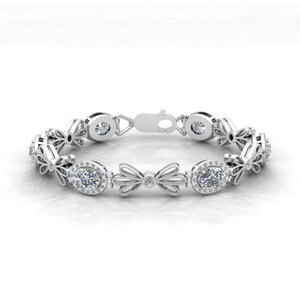 May include: A silver bracelet with a delicate bow design and oval-shaped gemstones. The bracelet is adorned with small, sparkling diamonds.