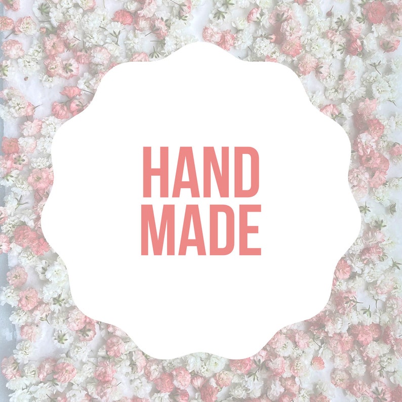 Puede incluir: Una forma blanca con bordes festoneados con las palabras "HAND MADE" en letras de bloque color coral. El fondo es un enfoque suave de flores blancas y rosas, creando una est&eacute;tica floral delicada.