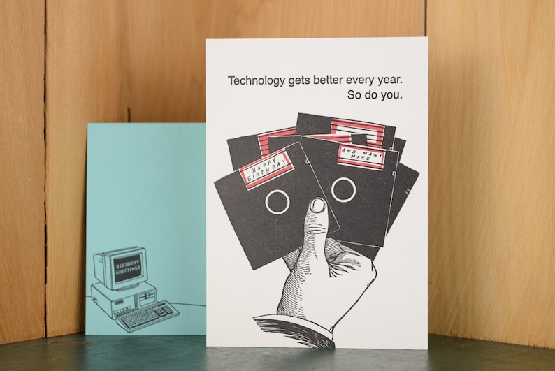 May include: A white card with black text that reads "Technology gets better every year. So do you."  A hand is holding a stack of five floppy disks. The top disk has red text that reads "Happy Birthday". The second disk has red text that reads "And Many More".