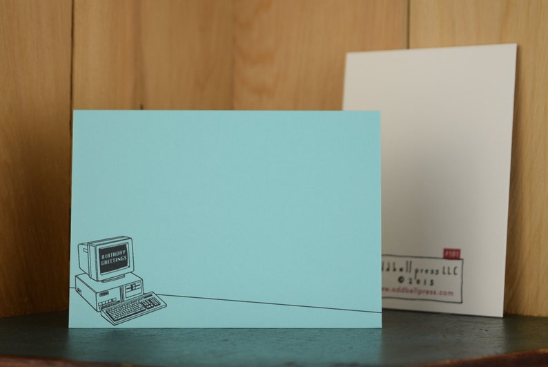 May include: A light blue card with a black and white illustration of a computer with the text "Birthday Greetings" on the screen. The card has a white border and the text "addallpress.com" in the bottom right corner.
