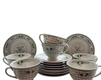 Puede incluir: Un juego de seis tazas de té y platillos blancos con un patrón floral en tonos verdes, marrones y rosas. Las tazas y los platillos tienen un diseño delicado y vintage.