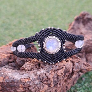 Könnte beinhalten: Ein schwarzes Makramee-Armband mit einem silberfarbenen runden Mondstein-Anhänger und weißen Perlen.