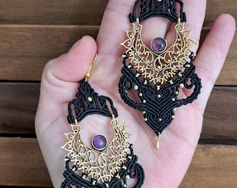 May include: A pair of long, black and gold earrings with intricate designs and purple gemstones. The earrings are made with macrame and feature a crescent moon shape.