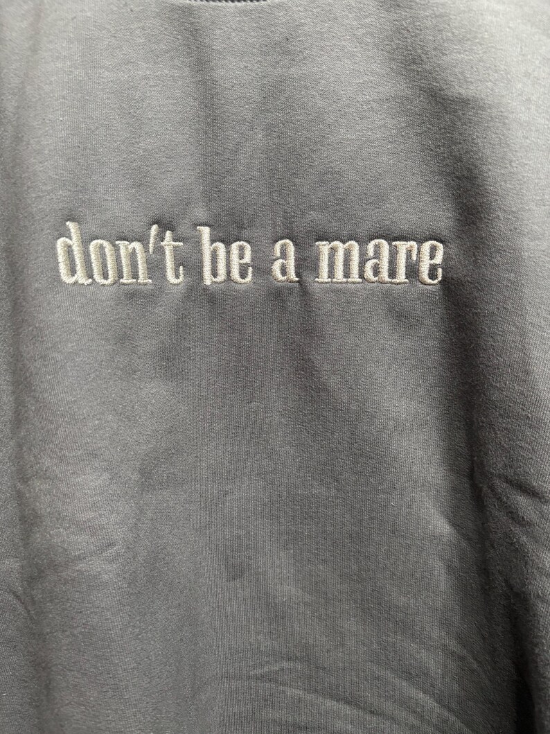 Puede incluir: Una sudadera gris con el texto "don't be a mare" bordado en blanco.