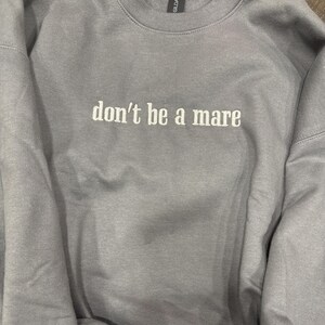 Puede incluir: Una sudadera gris con el texto "don't be a mare" bordado en blanco.