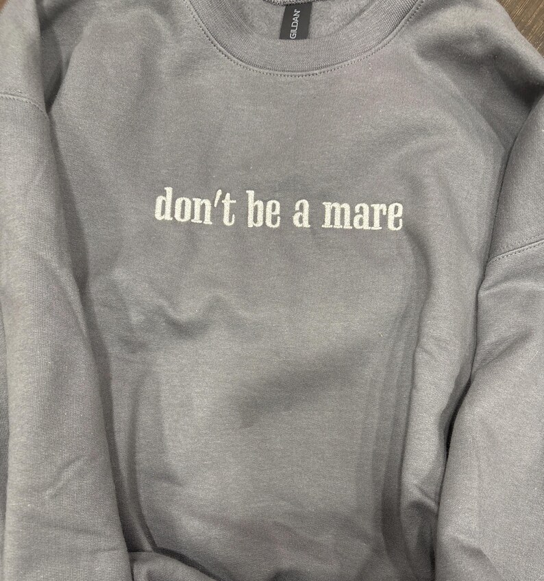 Puede incluir: Una sudadera gris con el texto "don't be a mare" bordado en blanco.