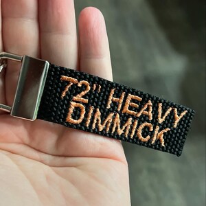 May include: A black key chain with a silver metal ring and a black strap with the text '72' HEAVY DIMMICK' embroidered in orange thread.