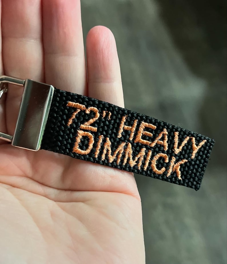 May include: A black key chain with a silver metal ring and a black strap with the text '72' HEAVY DIMMICK' embroidered in orange thread.