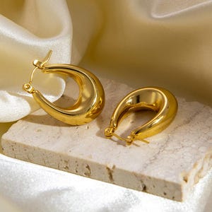 May include: A pair of gold hoop earrings with a thick, rounded shape. The earrings are made of a smooth, shiny metal.