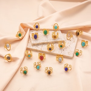 May include: A collection of gold rings with colorful gemstones. The rings feature a variety of stones, including turquoise, lapis lazuli, malachite, and tiger's eye.