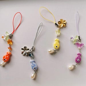 May include: Four colorful phone charms with fish, flower, and butterfly designs. Each charm has a different colored string and a pearl accent.