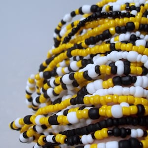 May include: Close-up of beaded strands in yellow, black, and white. The beads are small and round, creating a textured surface. The strands are intertwined, suggesting a woven or layered design. The color combination is striking and visually appealing.