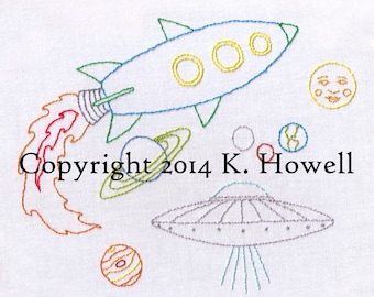 May include: Embroidered design of a blue rocket ship with yellow windows and a red flame, flying past a yellow moon with a face, a green planet with a ring, a red planet, and a gray UFO with blue beams. The text "Copyright 2014 K. Howell" is also embroidered on the white fabric.