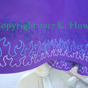 Può includere: Tessuto viola con un motivo a fiamma ricamato in bianco, blu e viola. Il tessuto ha il testo "Copyright 2017 K. Howell" ricamato.