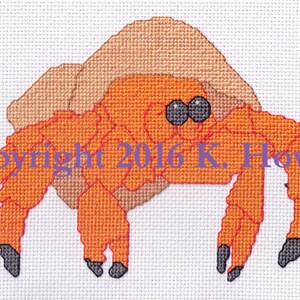 May include: Orange and brown cross-stitch pattern of a hermit crab carrying a shell on its back.